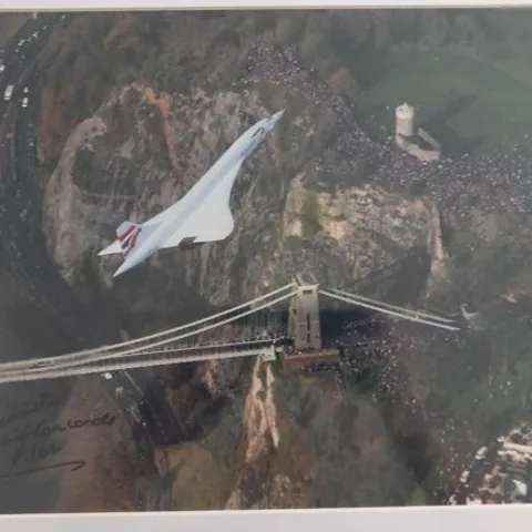 FRAMED AND MOUNTED PHOTOGRAPH OF  THE CONCORDE ON ITS LAST-EVER FLIGHT, OVER THE CLIFTON SUSPENSION BRIDGE IN BRISTOL, WESTERN ENGLAND BY LEWIS WHYLD SIGNED BY CHIEF PILOT CAPTAIN MIKE BANNISTER